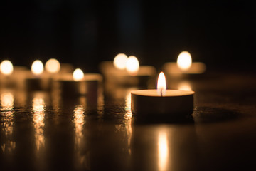 Small glowing candle on the floor on background of group of candles. Horizontal view