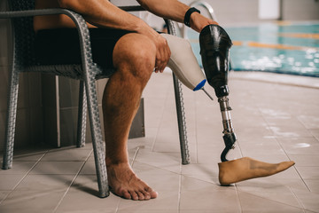 cropped shot of sportsman with artificial leg sitting on chair at indoor swimming pool