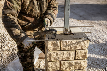 The worker is laying bricks on the fence