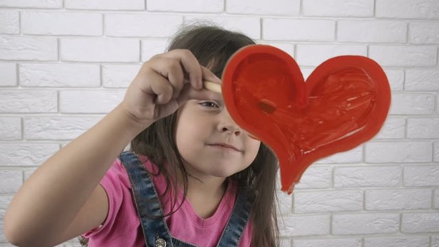 A child draws a heart. A little girl draws paint on the glass. A child draws a heart.