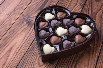 Heart shaped box with heart shaped dark and light chocolate truffles on wooden table