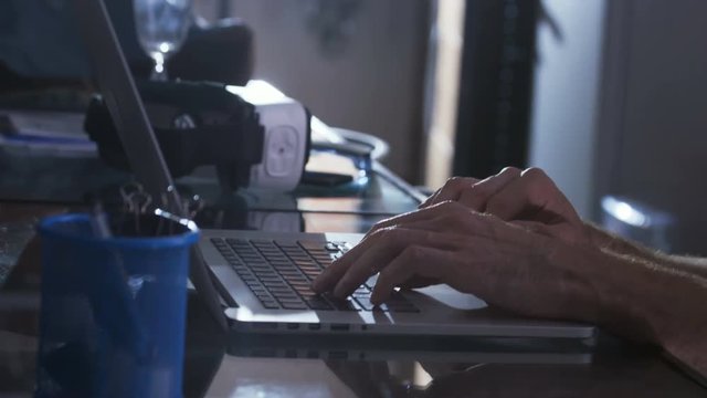 Person sitting at table, working. Indoors. Man in black balaclava breaking into corporate server. Cyber security.