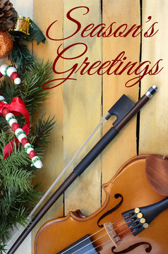 Christmas music theme with violine and bow on a rustic wooden background. Christmas decorations on one border. Vertical iimage with seasonal message added