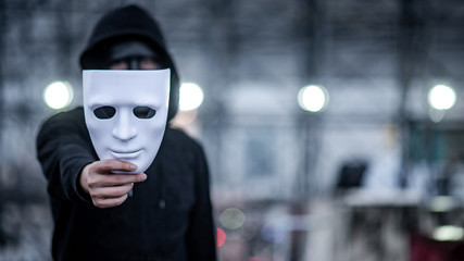 Mystery hoodie man with black mask holding white mask in his hand. Anonymous social masking or...