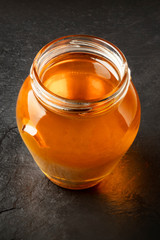 A photo of a jar of organic honey on a black background with copy space. Selective focus