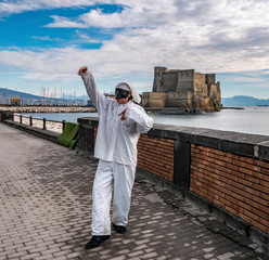 Pulcinella traditional Neapolitan mask gestures with Castel dell'Ovo in the background in the Gulf...
