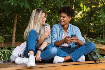 Happy young loving couple using mobile phone outdoors in park.