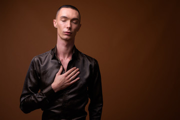 Fototapeta premium Młody przystojny biznesmen androgyniczny na brązowym tle