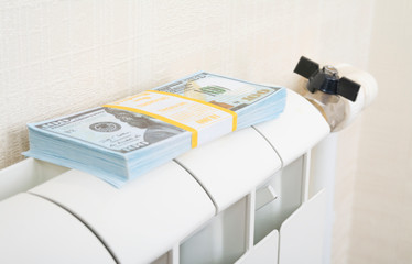 A bundle of money lies on the radiator with a closed valve. The concept of saving.