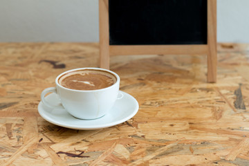 Obraz na płótnie Canvas A white cup of hot coffee on wooden table,A refreshment before work time or refreshment in relaxing time in a break with empty black board for write menu in coffee shop