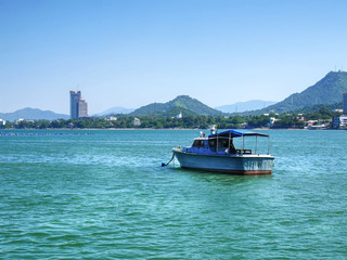 Naklejka premium Small Boat Floating in the Sea with Mountain and City on Background