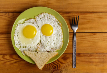 Scrambled eggs-fried eggs from 2 eggs slice of bread and a fork on plate on the table.