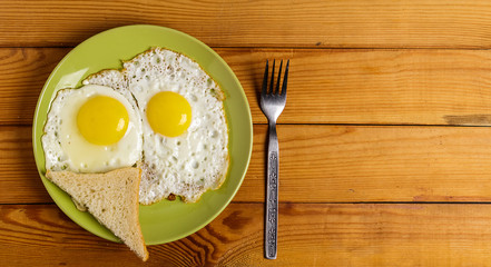 Scrambled eggs-fried eggs from 2 eggs slice of bread and a fork on plate on the table.