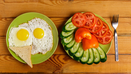 Fried eggs, pieces of vegetables, bread and fork on the table.