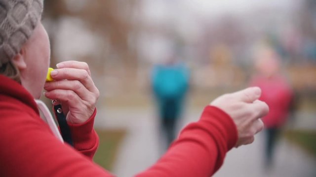 An old woman blows on whistle amd two elderly women starts walking on sticks of nordic walking. Slow motion