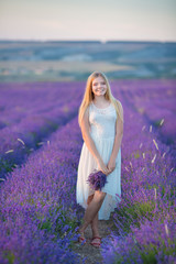 Fototapeta na wymiar Smiling beautiful blond lady model on lavender field enjoy summer day wearing airy whit dress with bouquet of flowers.