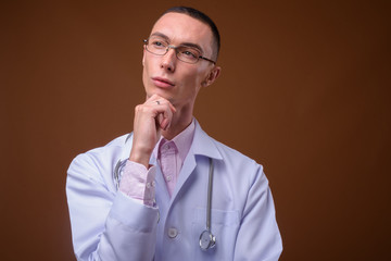 Young handsome androgynous man doctor against brown background