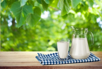 Glass of milk and jar on table with cloth and background
