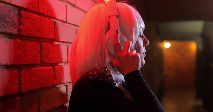 Sexy unusual girl in white wig listening to music using headphones, red light corridor