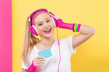 Woman in 1980's fashion holding a cassette tape on a split yellow and pink background