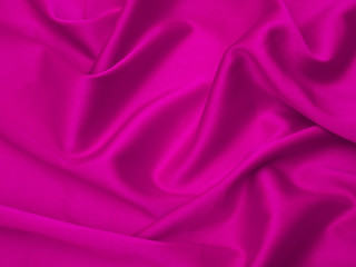 Pink fabric is laid out waves. Pink silk fabric for background or texture.