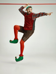 The happy smiling friendly man dressed like a funny gnome or elf hanging on an isolated gray studio...