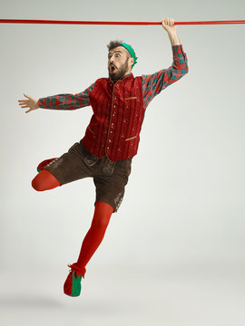 The Happy Smiling Friendly Man Dressed Like A Funny Gnome Or Elf Hanging On An Isolated Gray Studio Background. The Winter, Holiday, Christmas Concept