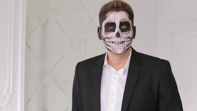 Portrait of man in suit with Halloween skull make-up showing his emotions. Devil makeup on face for halloween party. Death- painted male face. Businessman with make-up skeleton.