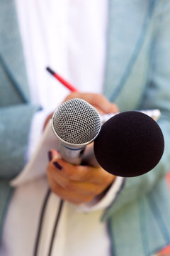 Female journalist at news conference, writing notes, holding microphone