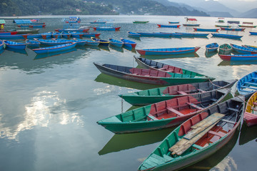 Fototapeta na wymiar Many multicolored wooden boats on the lake against the backdrop of green mountains. blue red green yellow empty boats on the water