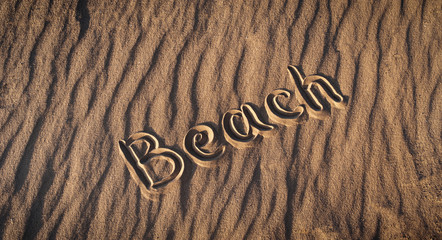 The word beach is written on the sand by hand. End of a beach season. Postcard. Shadows on the sand. South evening.
