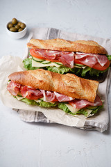 Side view of two fresh baguette sandwiches bahn-mi styled. Ham, sliced cheese, tomatoes and fresh...