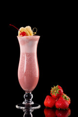 Glass of fresh strawberry milkshake decorated with cocktail cherry and banana slices isolated at black background.