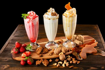 Fototapete Rund Three sweet milkshakes with nuts, caramel, strawberry and whipped cream at a wooden board on table background. © Mayatnikstudio