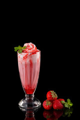Glass of fresh strawberry milkshake decorated with mint and syrup isolated at black background.
