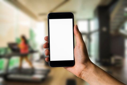 Mockup image of hand holding white mobile phone with blank white screen in the gym.