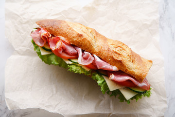 Fresh baguette sandwich bahn-mi styled. Ham, sliced cheese, tomatoes and fresh lettuce in wrapping...
