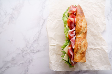 Fresh baguette sandwich bahn-mi styled. Ham, sliced cheese, tomatoes and fresh lettuce in wrapping...