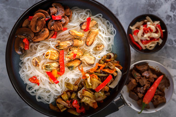 Traditional Asian food - rice noodles with seafood, salad, red pepper and fried mushrooms are on the side table. Close-up. Top view