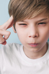 Boy jokingly shows piercing glance, holding index fingers at temples