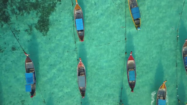 Top of traditional Thai boats, white sand beach, beautiful clear emerald sea, seen from camera down forward moving high aerial drone view on tropical island, Ko Lipe, Thailand.