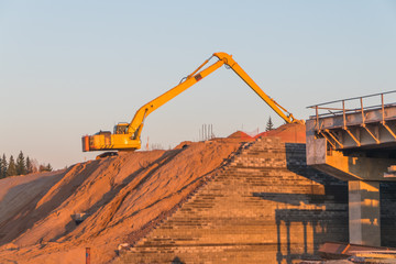 the construction of the road, an excavator on a mountain of sand