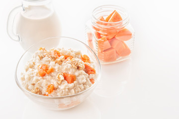 Oatmeal with pumpkin and nuts in a glass plate, a jug of milk and sliced carrots in a jar on a...