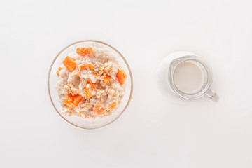 Fototapeta na wymiar Oatmeal with pumpkin and nuts in a glass plate and a jug with milk on a white background. Copy space. Top view