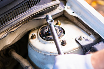 Support absorber car. Close-up hand specialist unscrews the nut from the stem with a socket wrench.