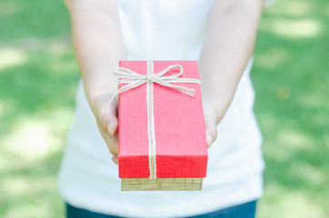 beautiful woman hand give me a red gift box celebration greeting for holiday, merry christmas, happy new year and birthday on standing in the park with blur green nature bokeh background.