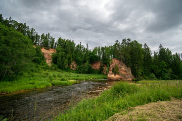 rocky stream of river deep in forest in summer green weather with sandstone cliffs