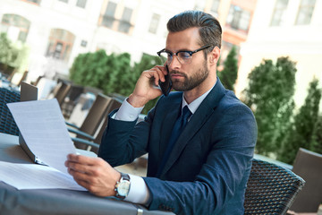 Young businessman with a beard and wearing glasses sitting in a cafe working on a contract