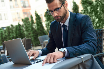 Young businessman with a beard and wearing glasses sitting in a cafe working on a contract