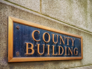 Exterior sign that reads "County Building" in brass letters. Graphic resource.